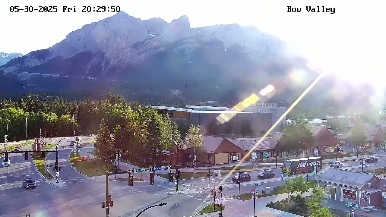 A sunny, high-angle view of a mountain range overlooking a town's intersection with several buildings and vehicles.