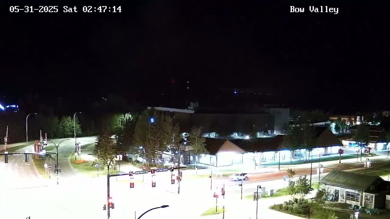 A nighttime aerial view of a road intersection with buildings and trees, under a clear sky.