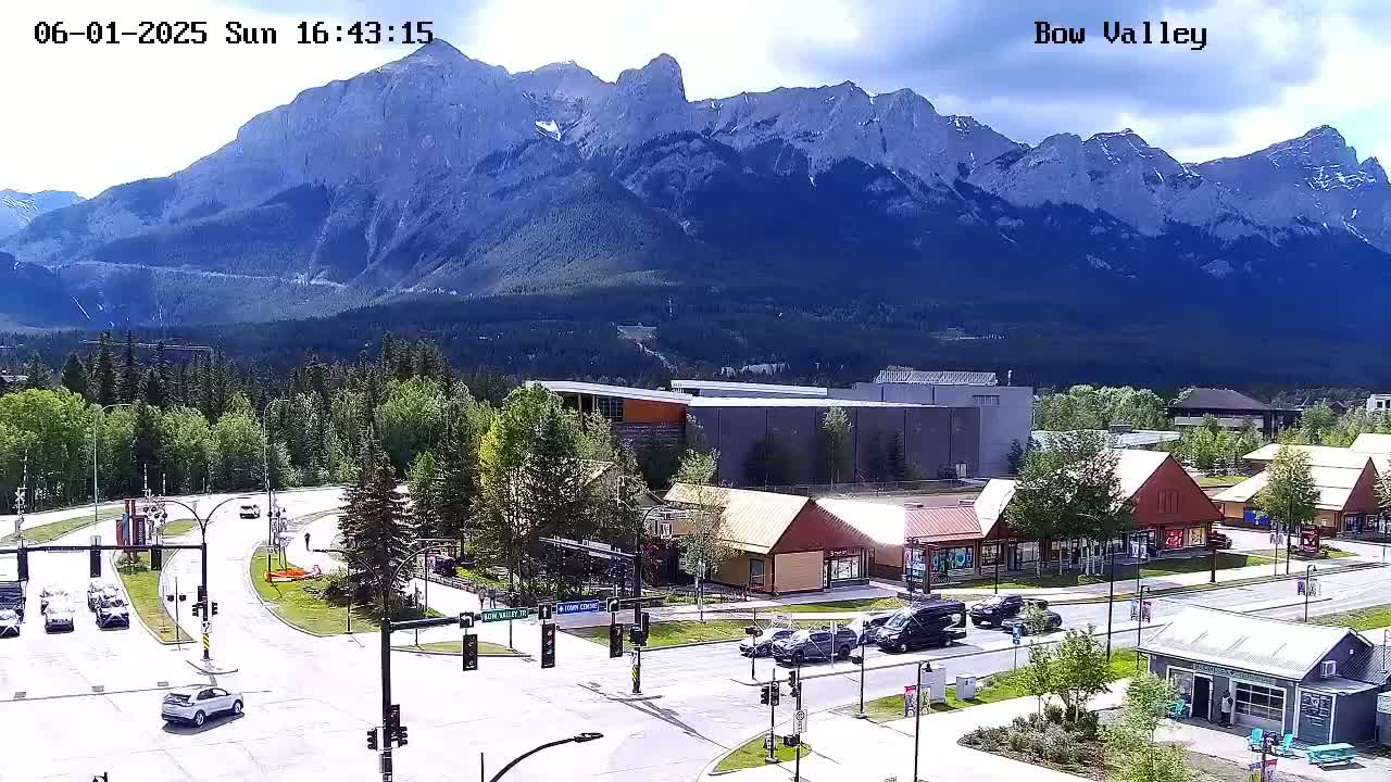 A partly sunny day shows a mountain range in the background overlooking a town with a road intersection and several buildings, including small shops and restaurants.