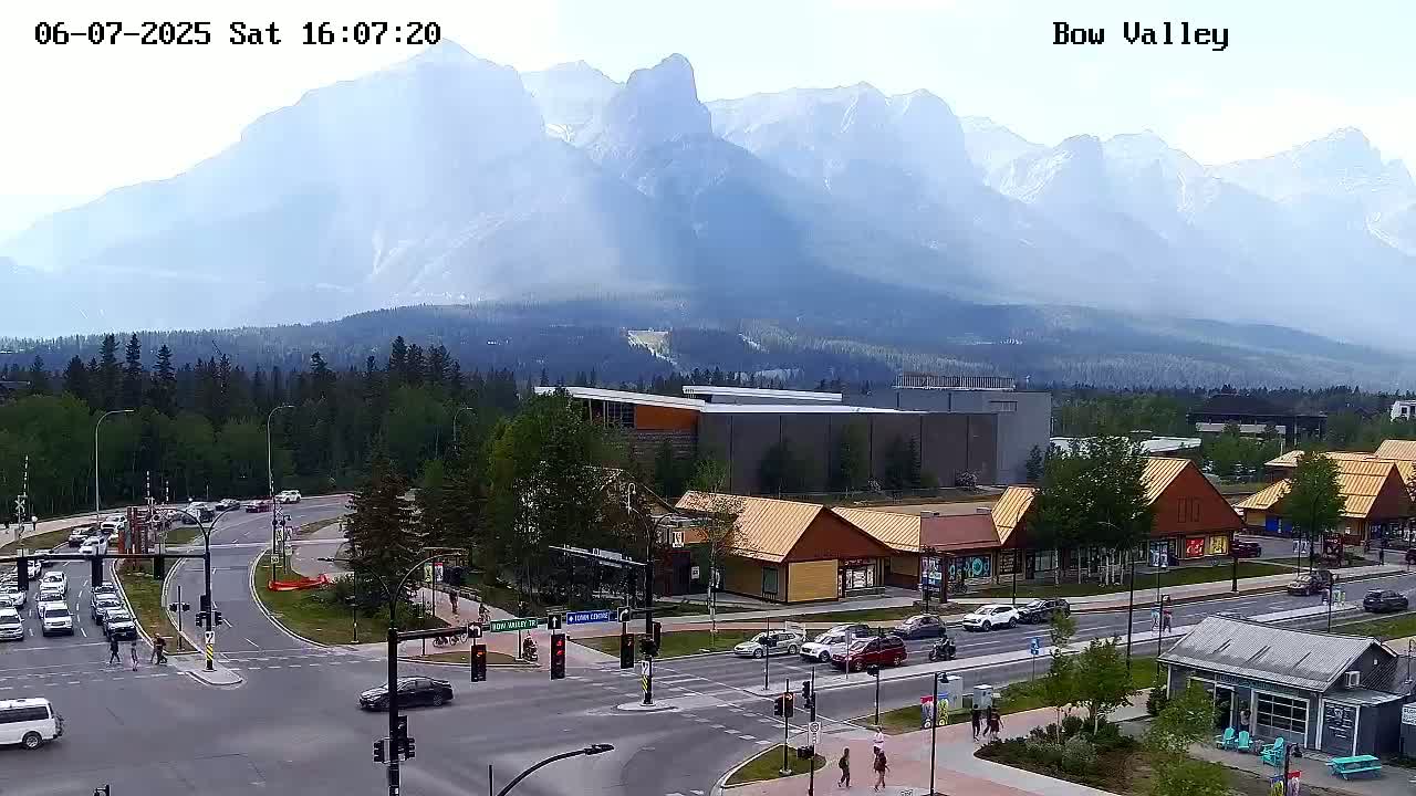 A hazy view of a mountain range behind a town with buildings and roads, and some pedestrians and cars are visible.