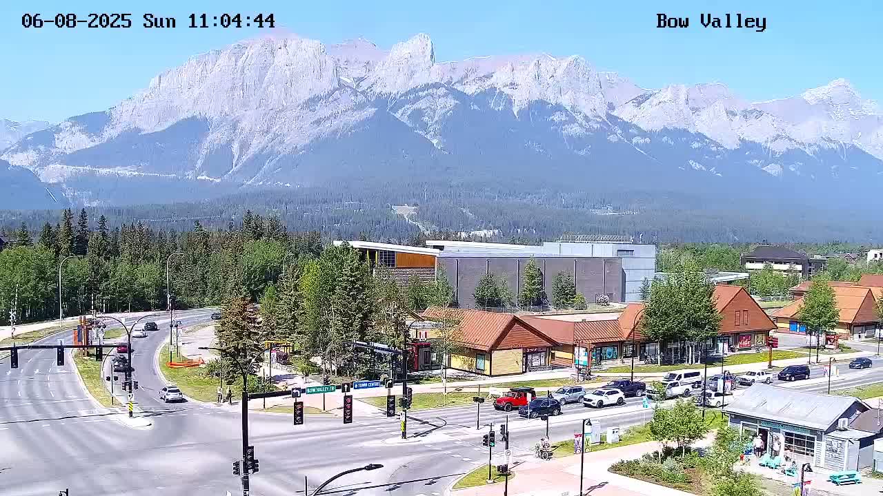 A sunny day reveals a mountain range in the background, overlooking a town with roads, buildings, and cars.