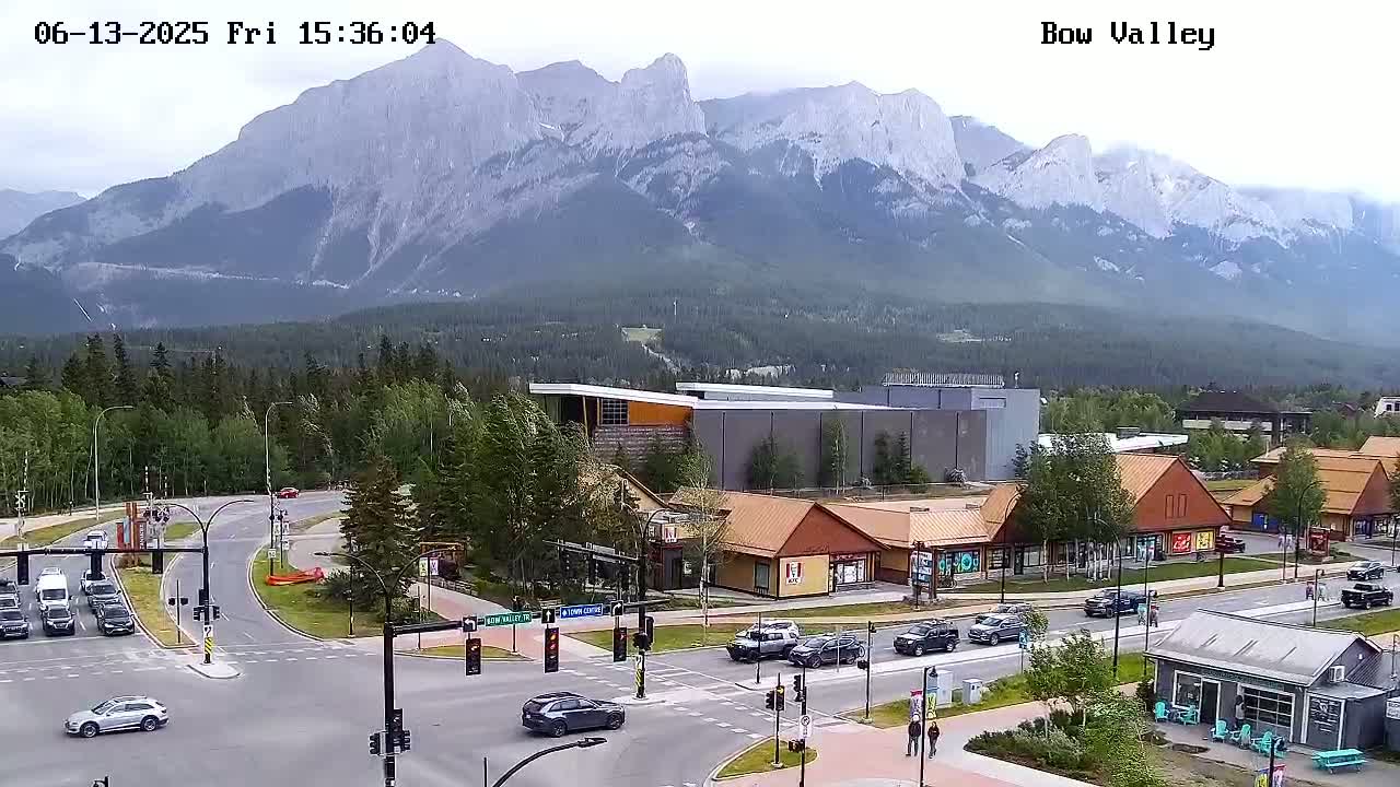 A partly cloudy day reveals a mountain range in the background of a town intersection with several cars and buildings, including a KFC.