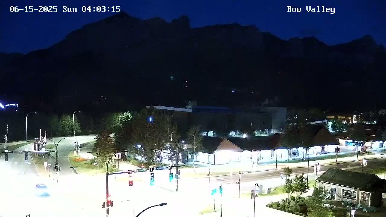 A nighttime view of a road intersection and buildings near a mountain under a clear, dark sky.