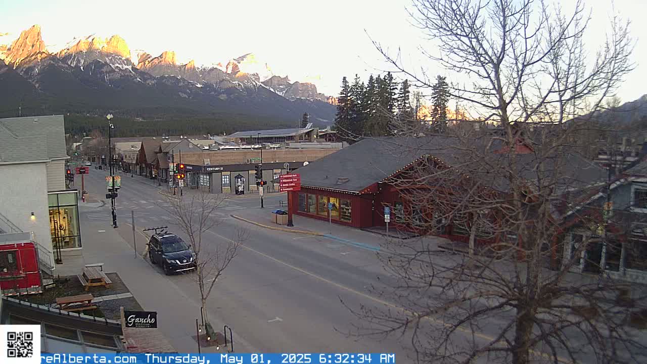 A mostly empty street in a town nestled at the base of snow-capped mountains at sunrise.
