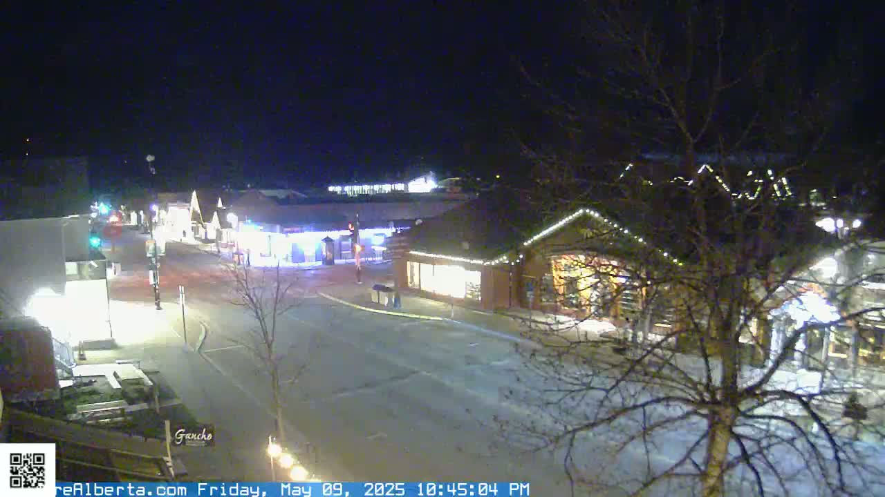 A nighttime, snow-covered street scene shows illuminated buildings and sparsely trafficked roads.