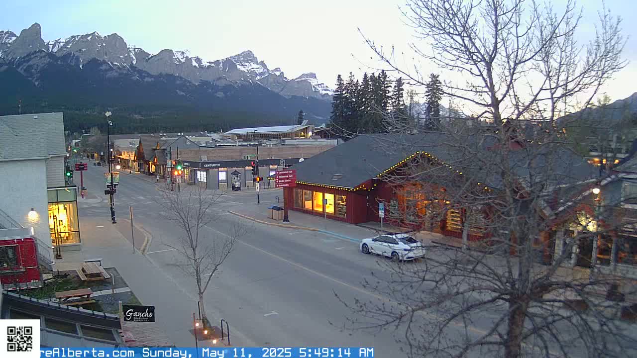 A mostly empty street lined with shops and buildings under a twilight sky, with snow-capped mountains in the background.