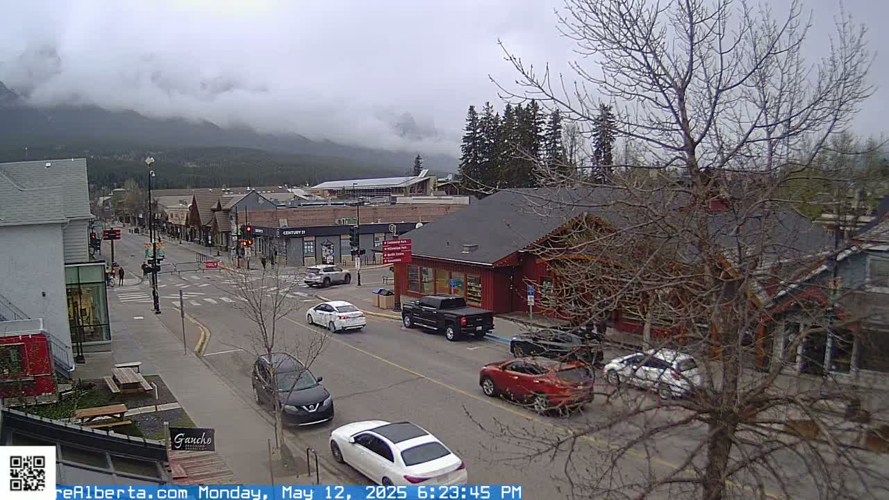 A cloudy day reveals a mountain range in the distance overlooking a town street with several cars and buildings.