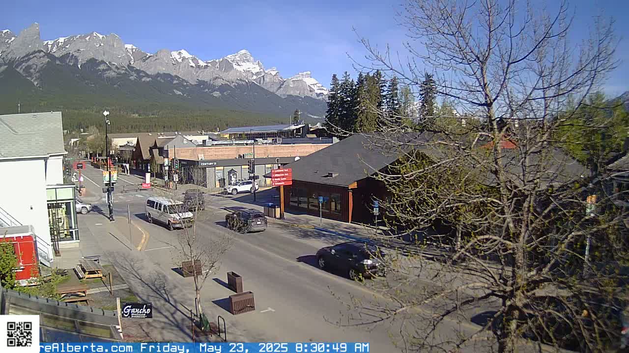 A sunny street scene shows a town nestled at the base of snow-capped mountains.