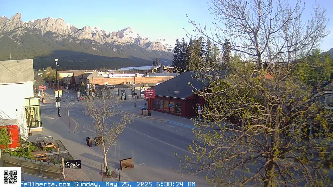 A mostly empty street scene in a town nestled at the base of a snow-capped mountain range on a clear, sunny morning.
