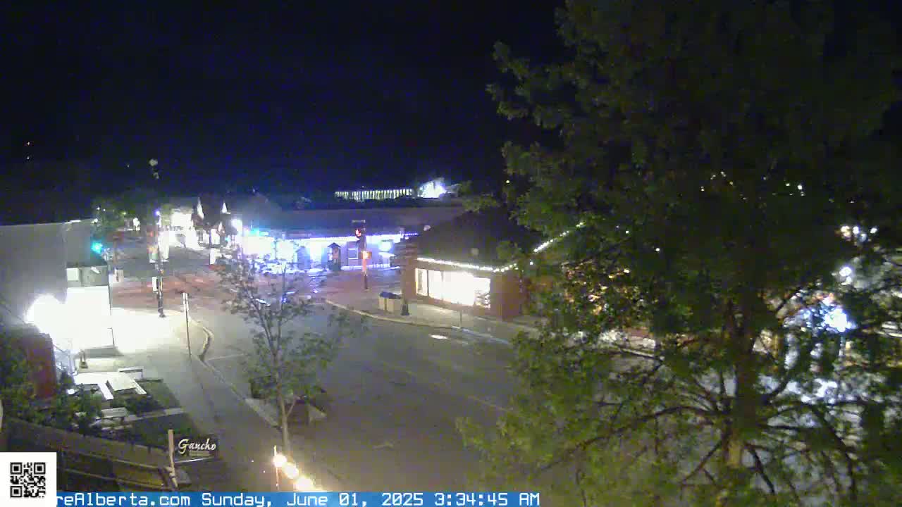 A nighttime, high-angle view of a quiet town square with illuminated buildings and streetlights.