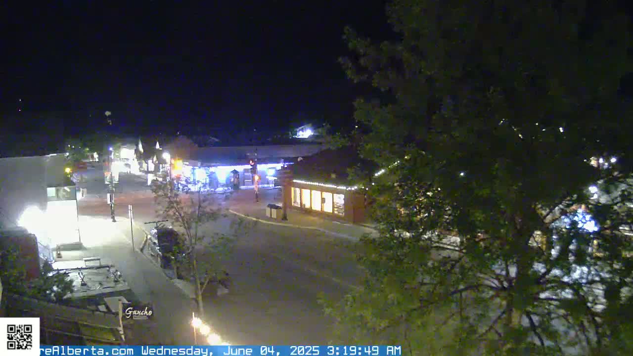 A nighttime, high-angle view of a quiet town square with illuminated buildings and trees.
