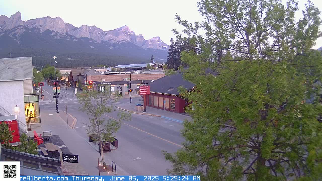 A mostly empty street in a town nestled at the base of a mountain range under a partly cloudy sky.
