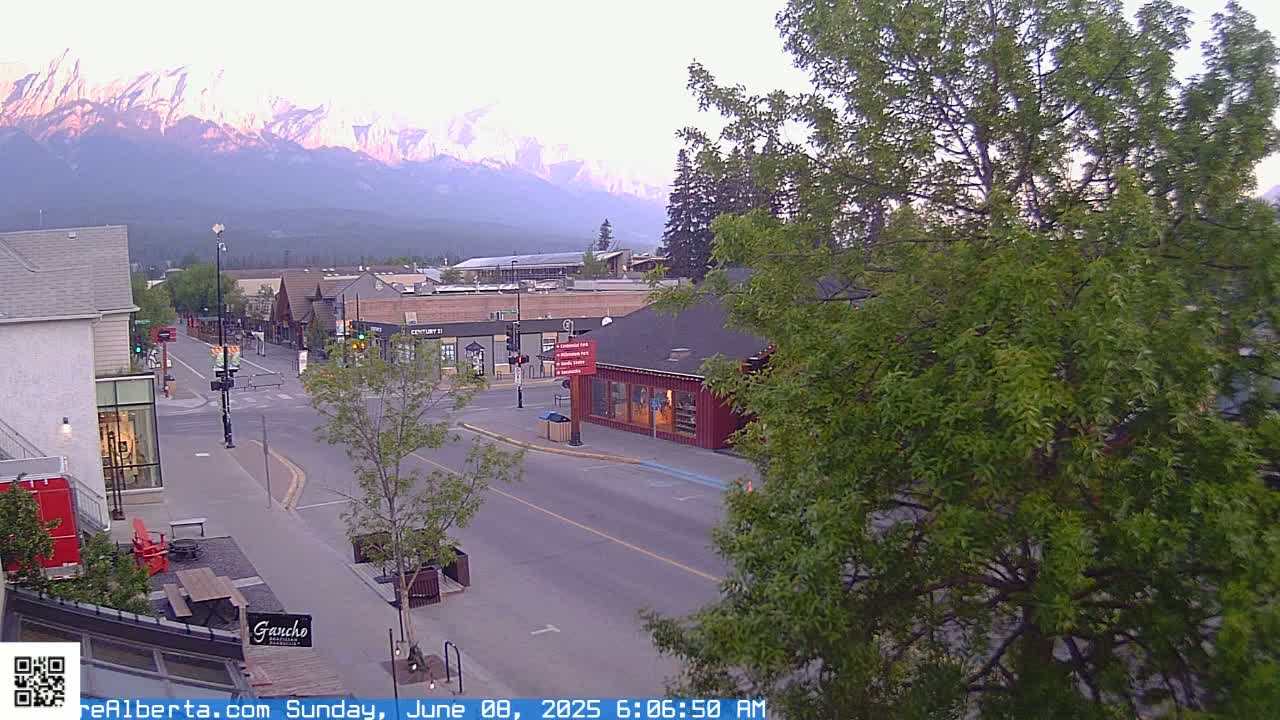 A mostly empty street in a town at sunrise, with mountains in the background under a clear sky.