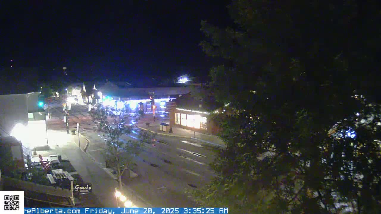 A nighttime, overhead view of a mostly empty street in a town, with some buildings and trees visible.