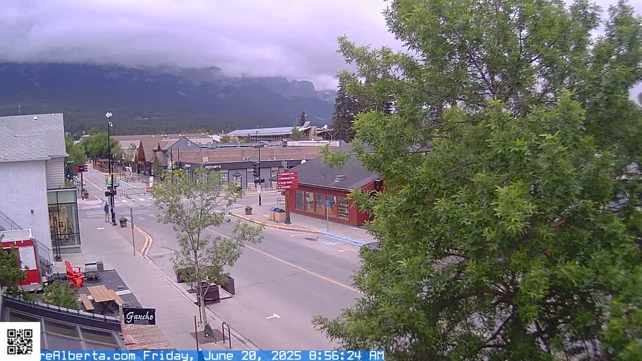 A mostly cloudy day reveals a quiet street scene in a town nestled at the base of mountains.