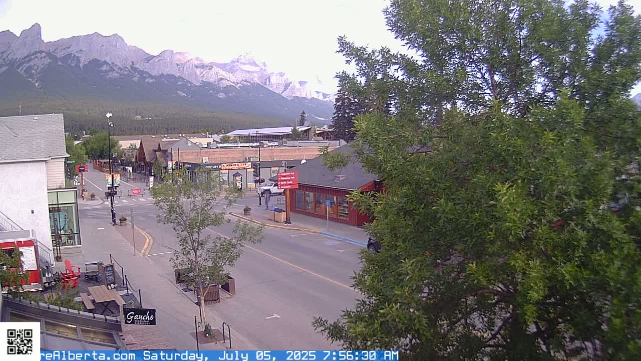 A mostly clear, overcast day reveals a mountain range in the background of a quiet town street with small shops and buildings.