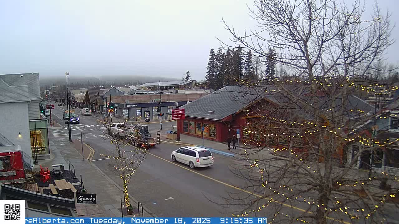 A nighttime street scene shows wet roads and buildings with lights on under a dark sky.