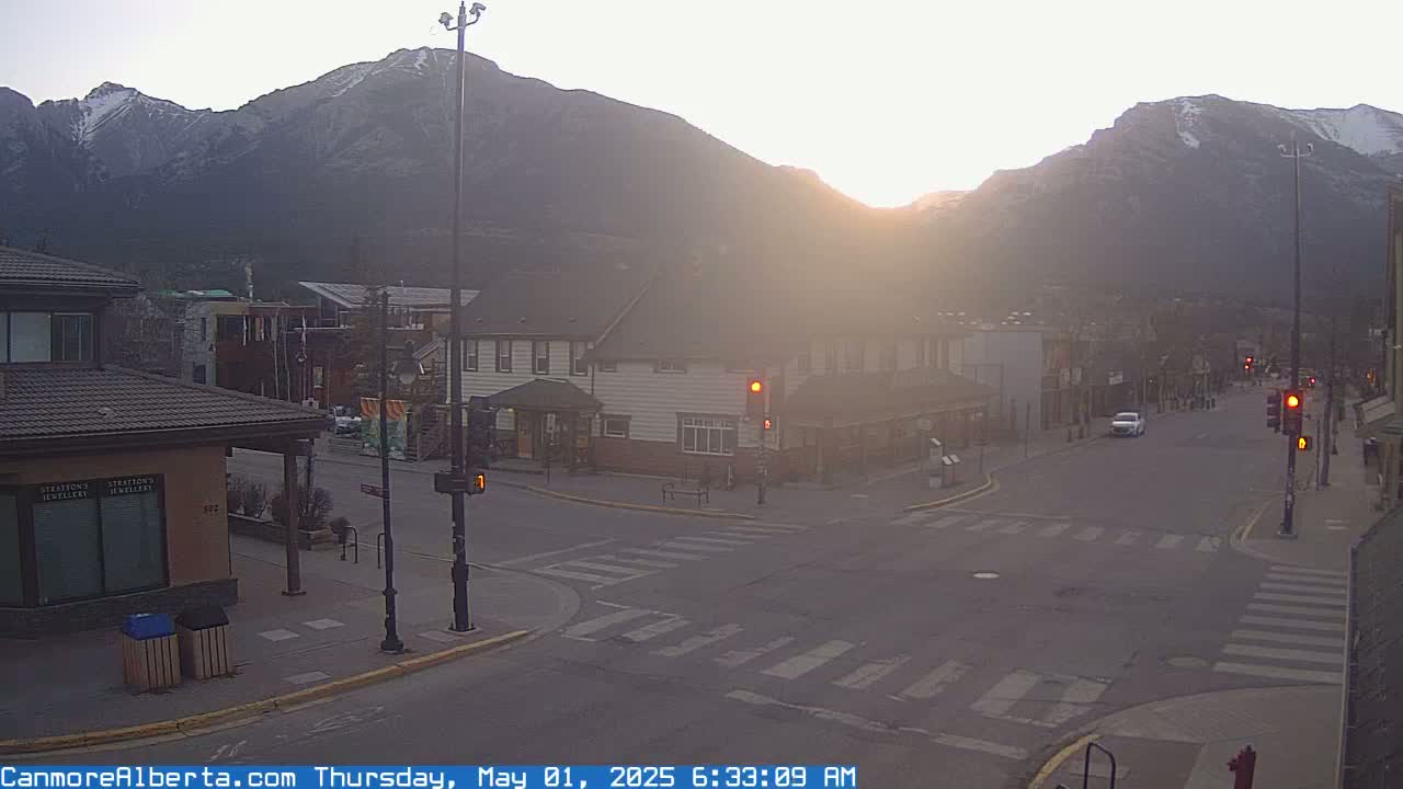 A hazy sunrise illuminates a quiet town square nestled against snow-capped mountains.