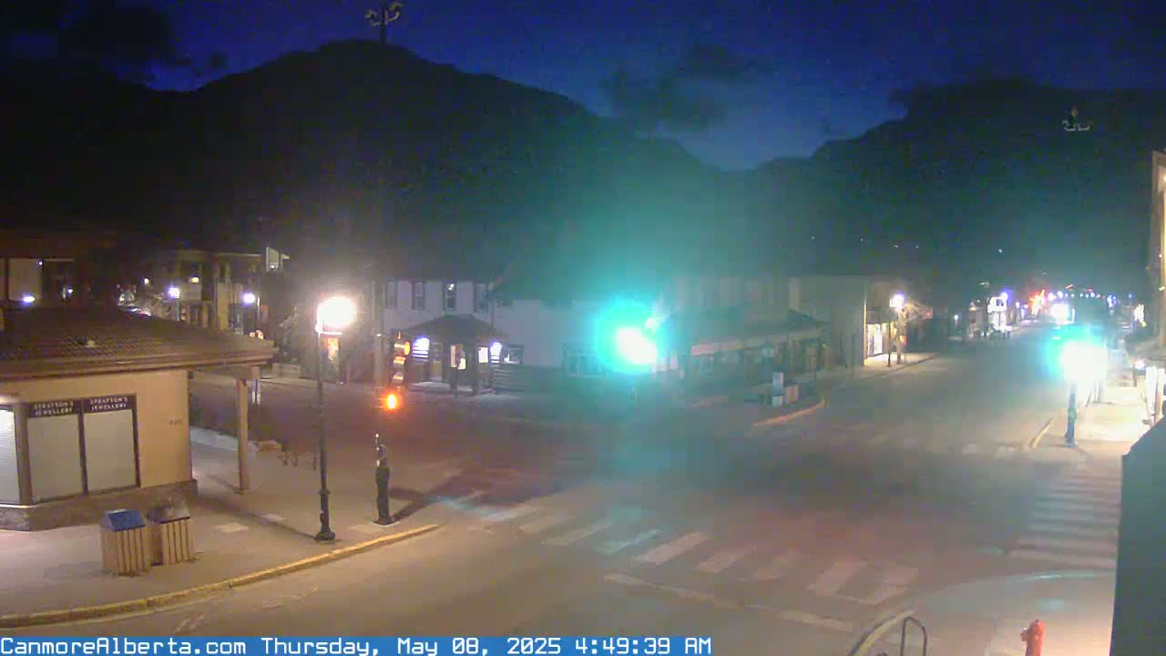 A nighttime street scene in a town nestled against a dark mountain, under a mostly clear sky.