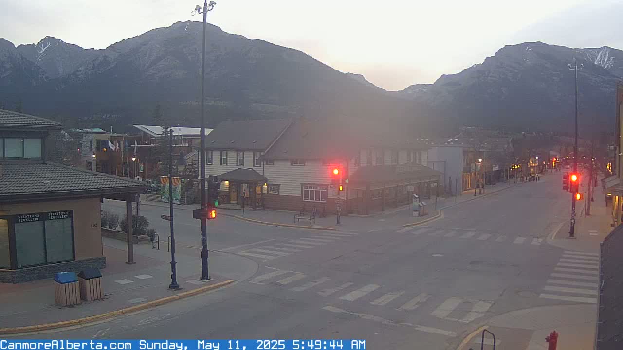A mostly empty street in a town at dawn, with mountains in the background under an overcast sky.
