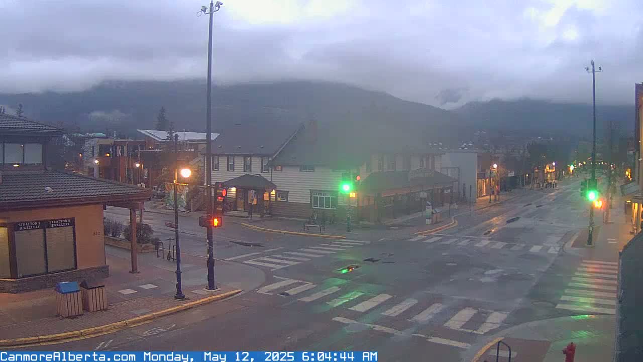 A mostly empty street in a town, under a cloudy, overcast sky, with mountains visible in the background.