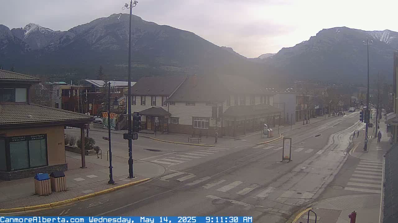 A hazy, overcast morning view of a town's main street, with snow-capped mountains in the background.