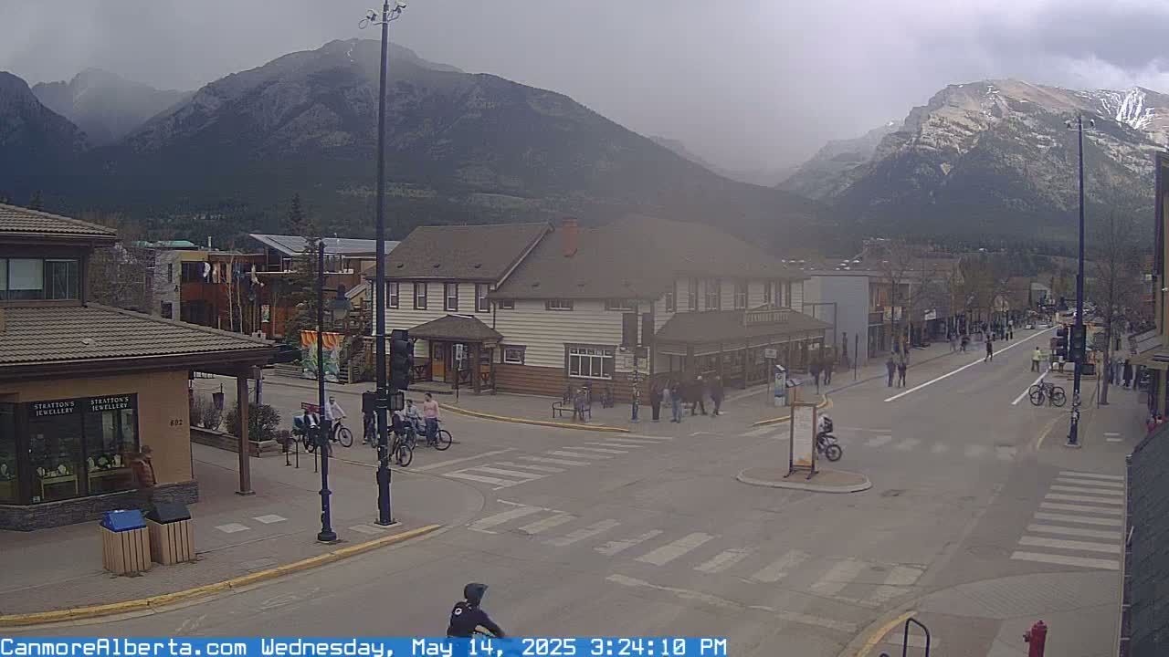 A hazy, overcast day reveals a town street scene with pedestrians and cyclists at an intersection, nestled against a backdrop of mountains.