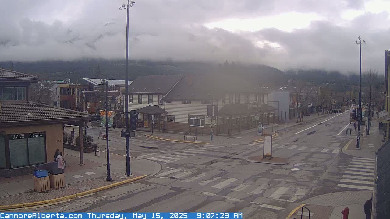 A cloudy day reveals a town's street intersection with buildings and mountains shrouded in mist in the background.