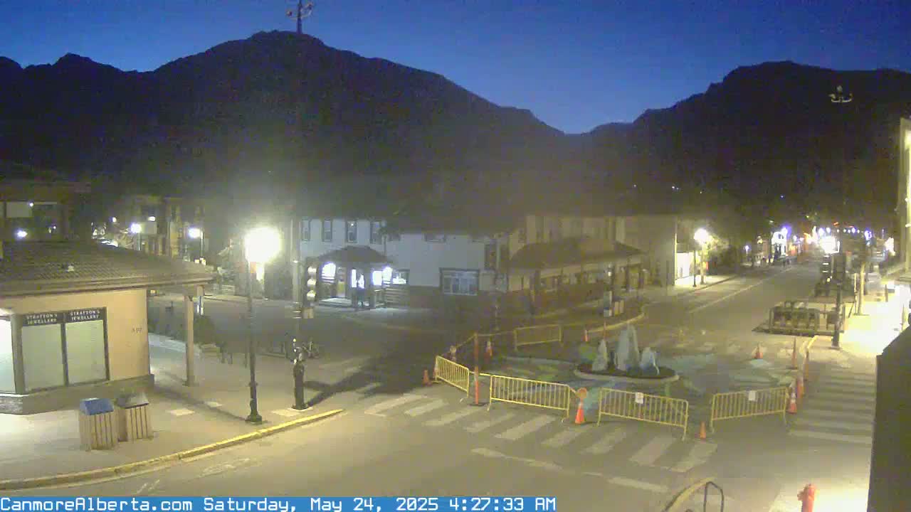 A nighttime street scene in a town nestled against a mountain range under a clear, dark sky.