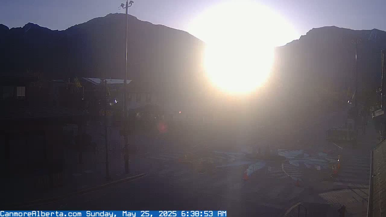 A hazy sunrise illuminates a town square nestled in a valley between mountains.