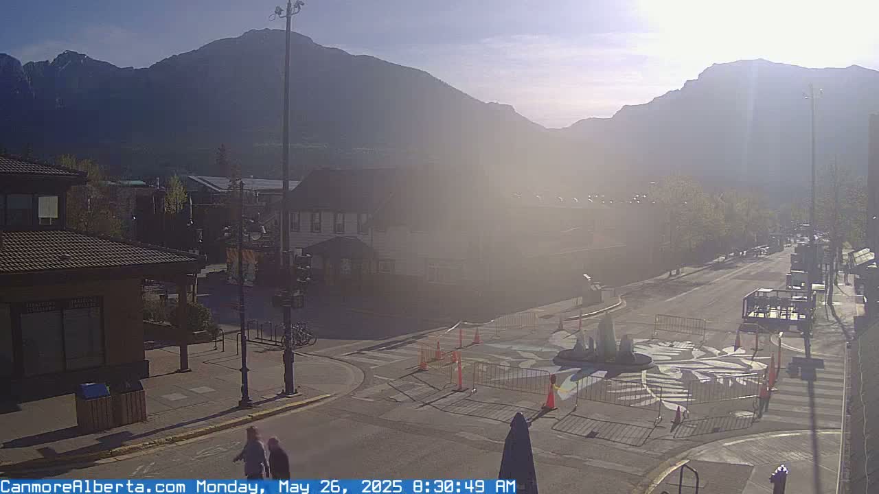 A hazy, sunny morning scene shows a town square with a street intersection, buildings, and mountains in the background.