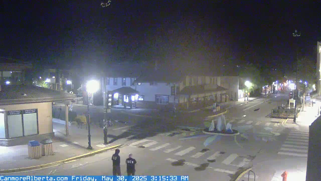 A nighttime view of a town square with two people standing near a crosswalk, under a clear sky.