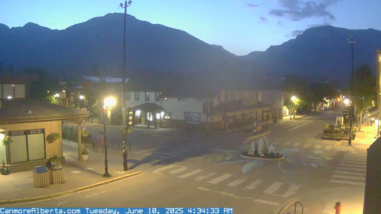A dimly lit town square at dusk, nestled against a backdrop of dark mountains under a twilight sky.