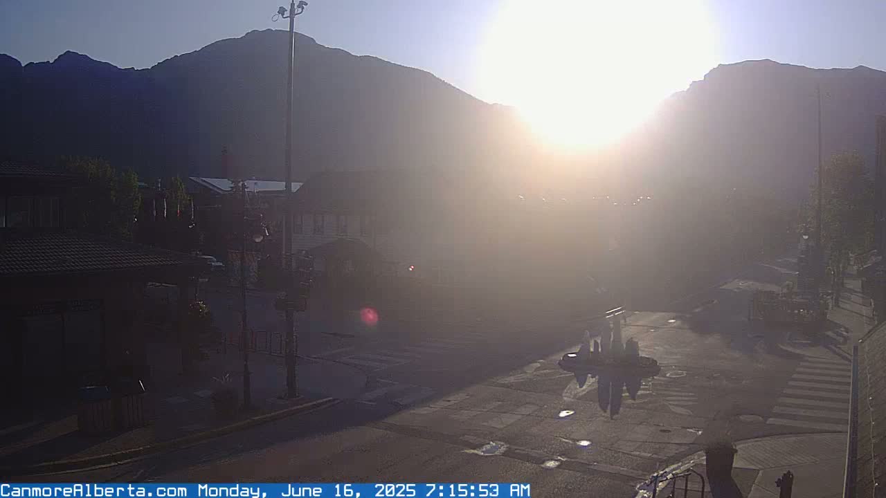 A hazy sunrise illuminates a town square nestled against a mountain range.