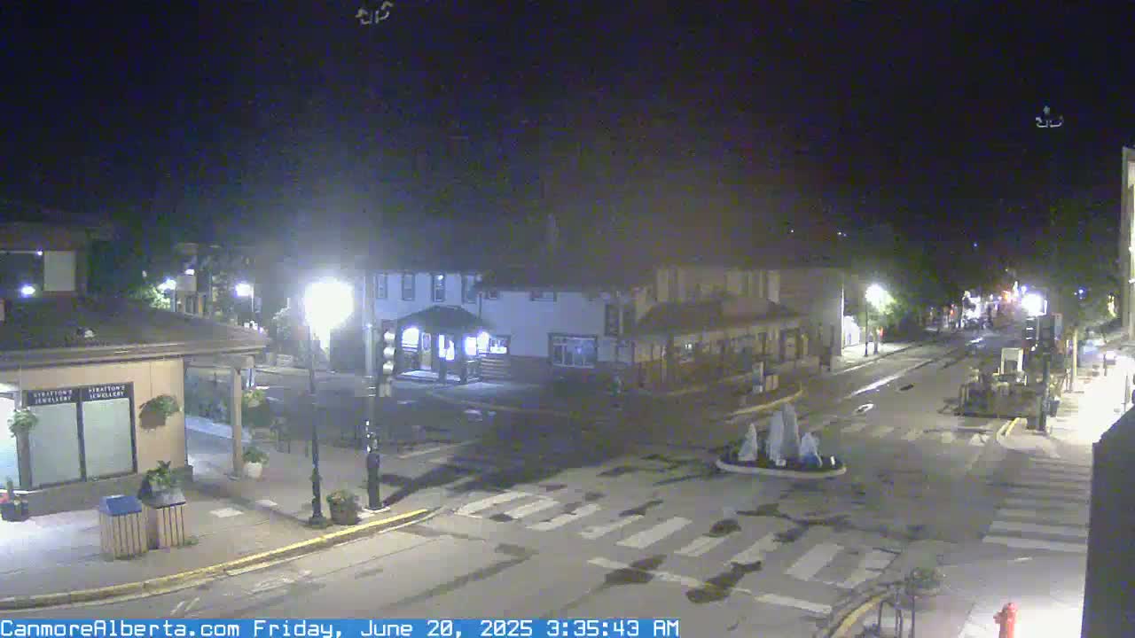 A nighttime view of a quiet town square with several buildings and a crosswalk, under clear skies.