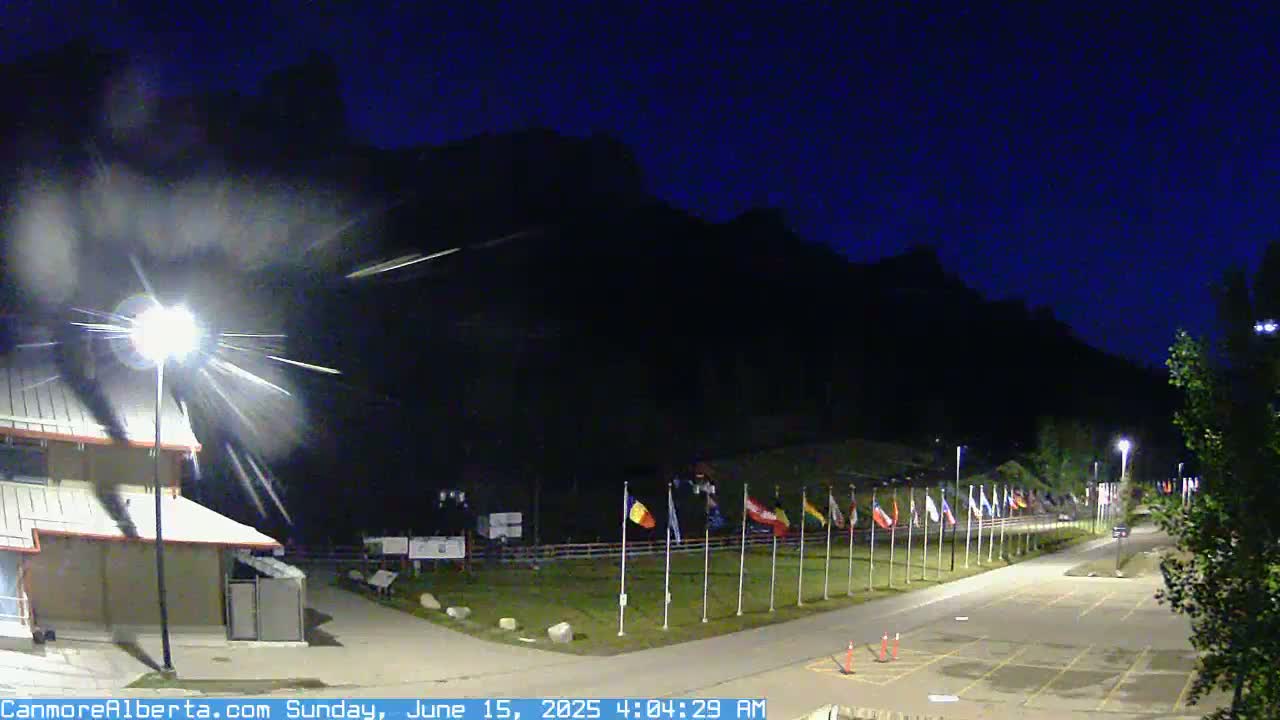 A nighttime view of a row of flags in front of a building, with mountains in the background under a dark, clear sky.