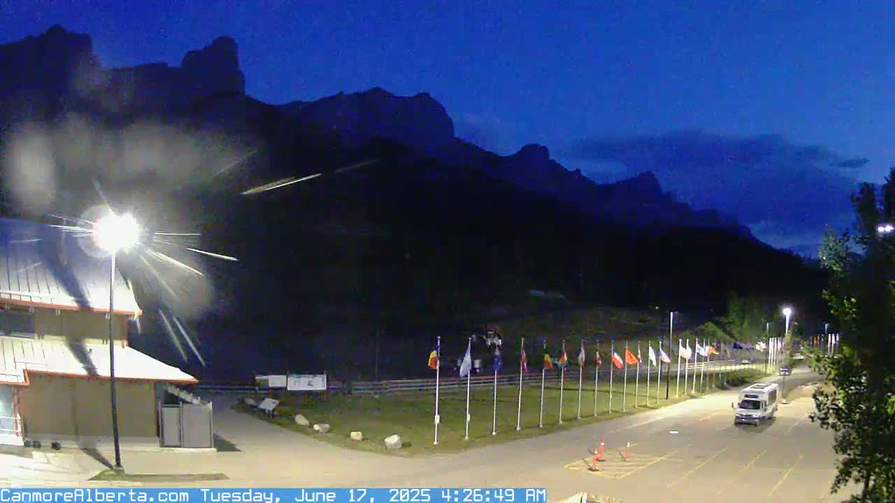 A row of flags stands in front of a dark mountain range under a twilight sky.