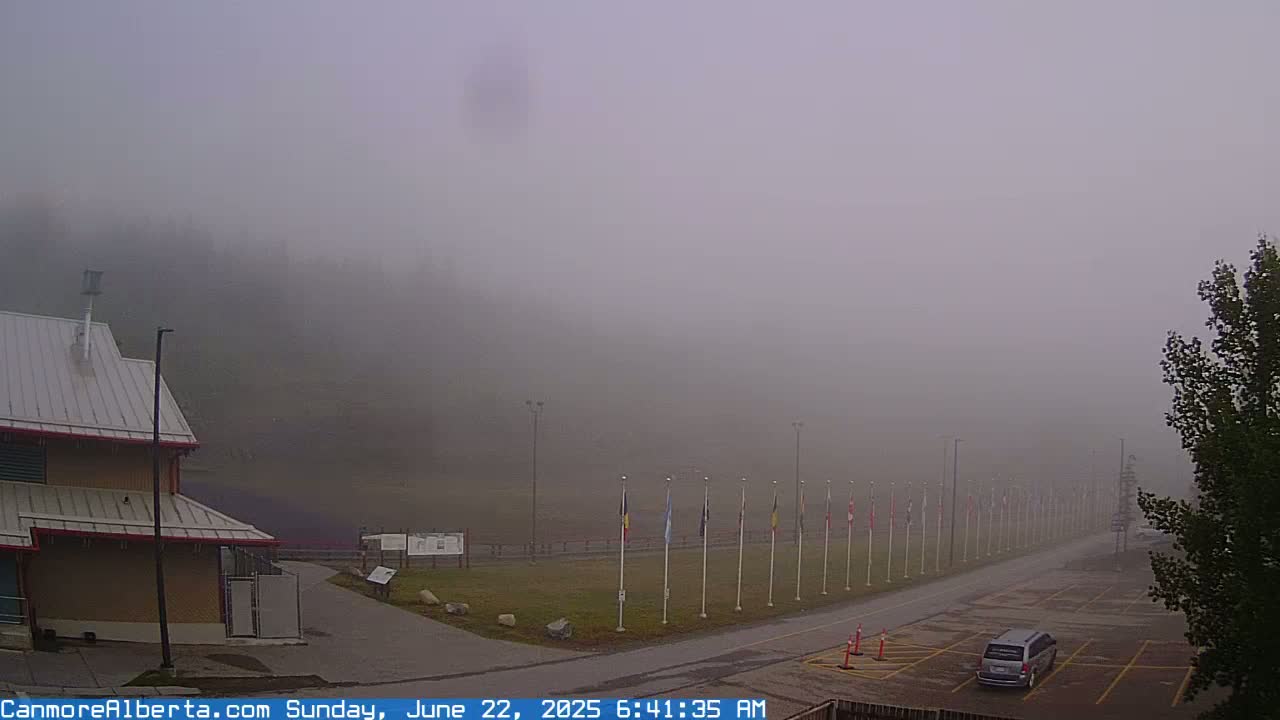 A foggy parking lot with a building, a row of flags, and a single vehicle is visible.