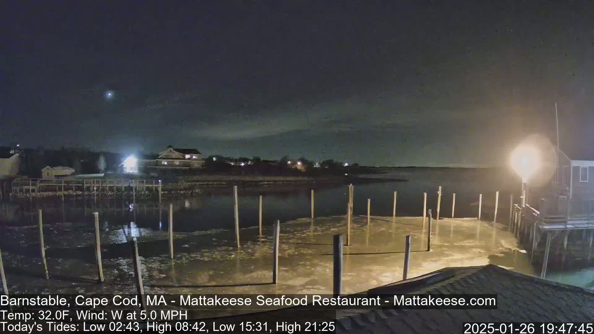 A nighttime view of a partially frozen dock and calm water, under a clear, dark sky.