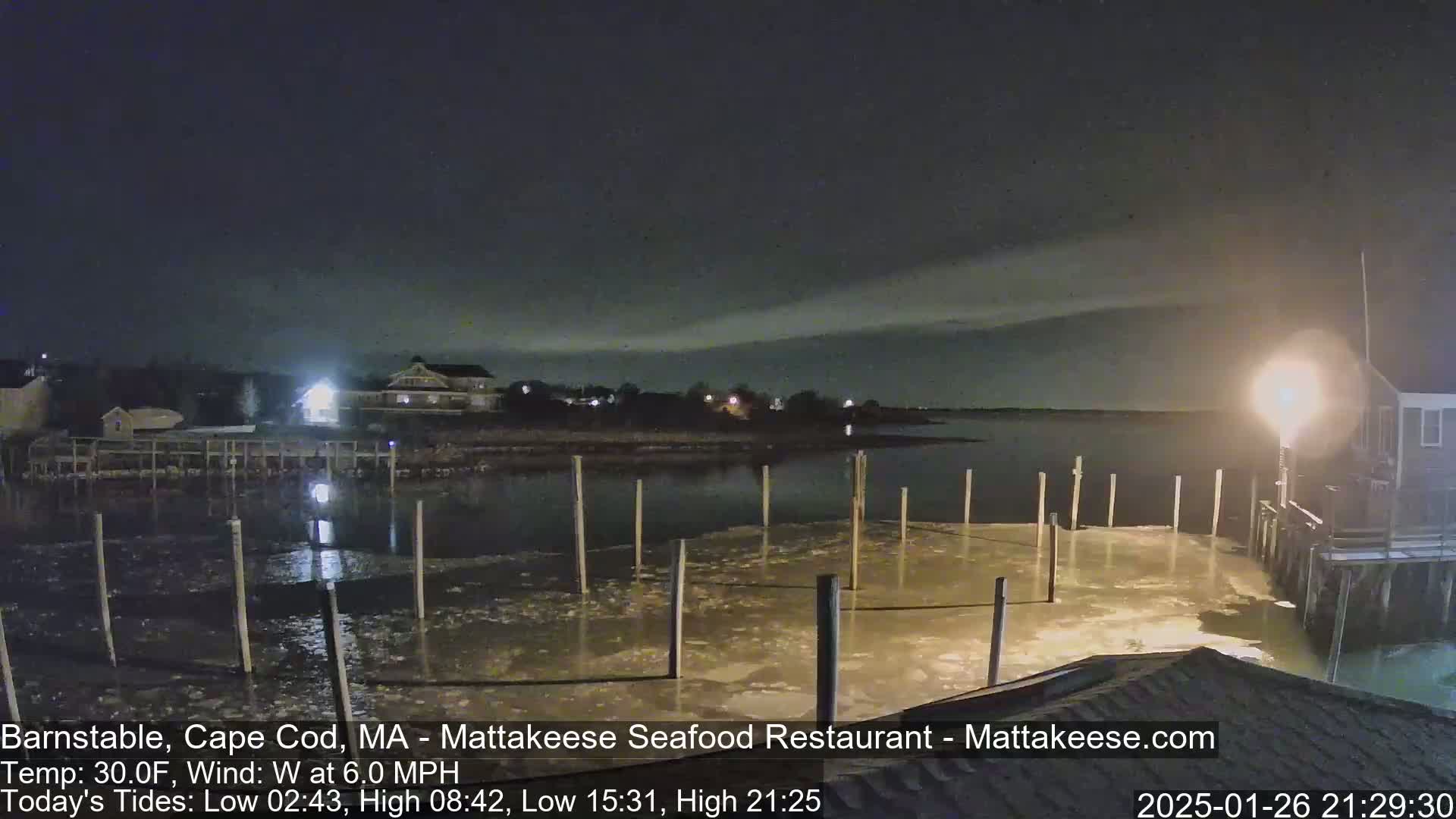 A nighttime view of a partially frozen dock on a calm body of water, under a cloudy sky.