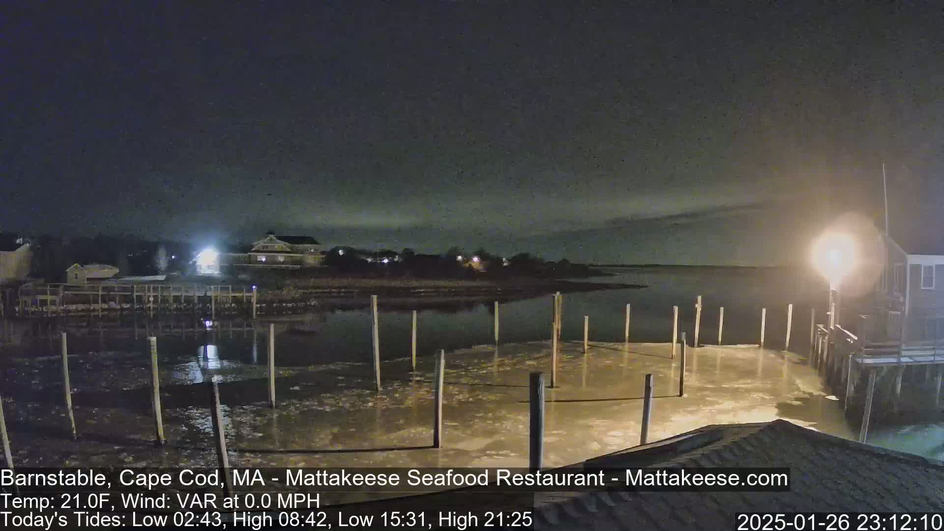 A nighttime view of a partially frozen harbor with wooden pilings and buildings in the background under a dark, clear sky.