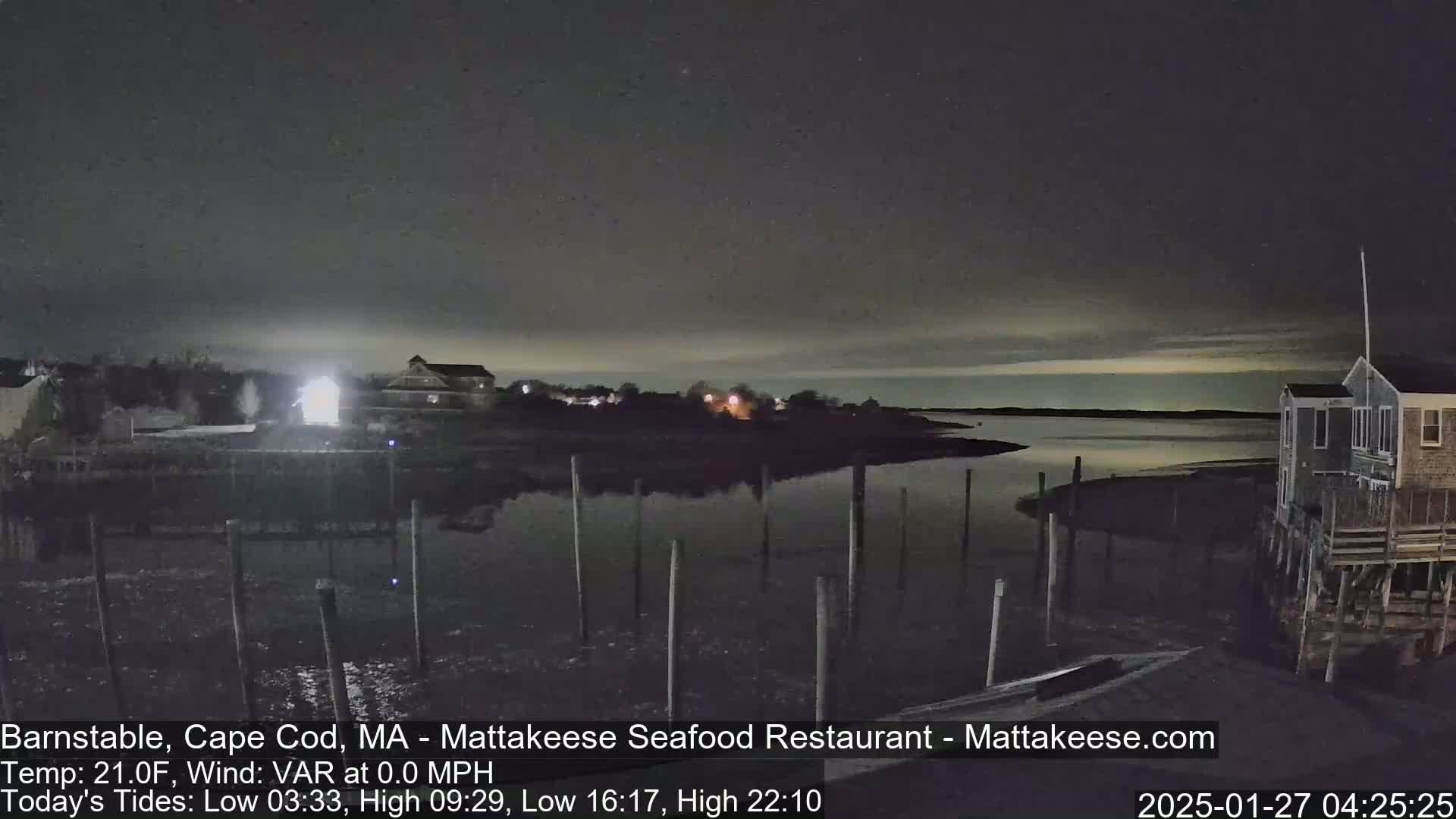 Here is a description of the image: A nighttime view of a calm body of water with a few buildings and docks visible under a dark, mostly clear sky.