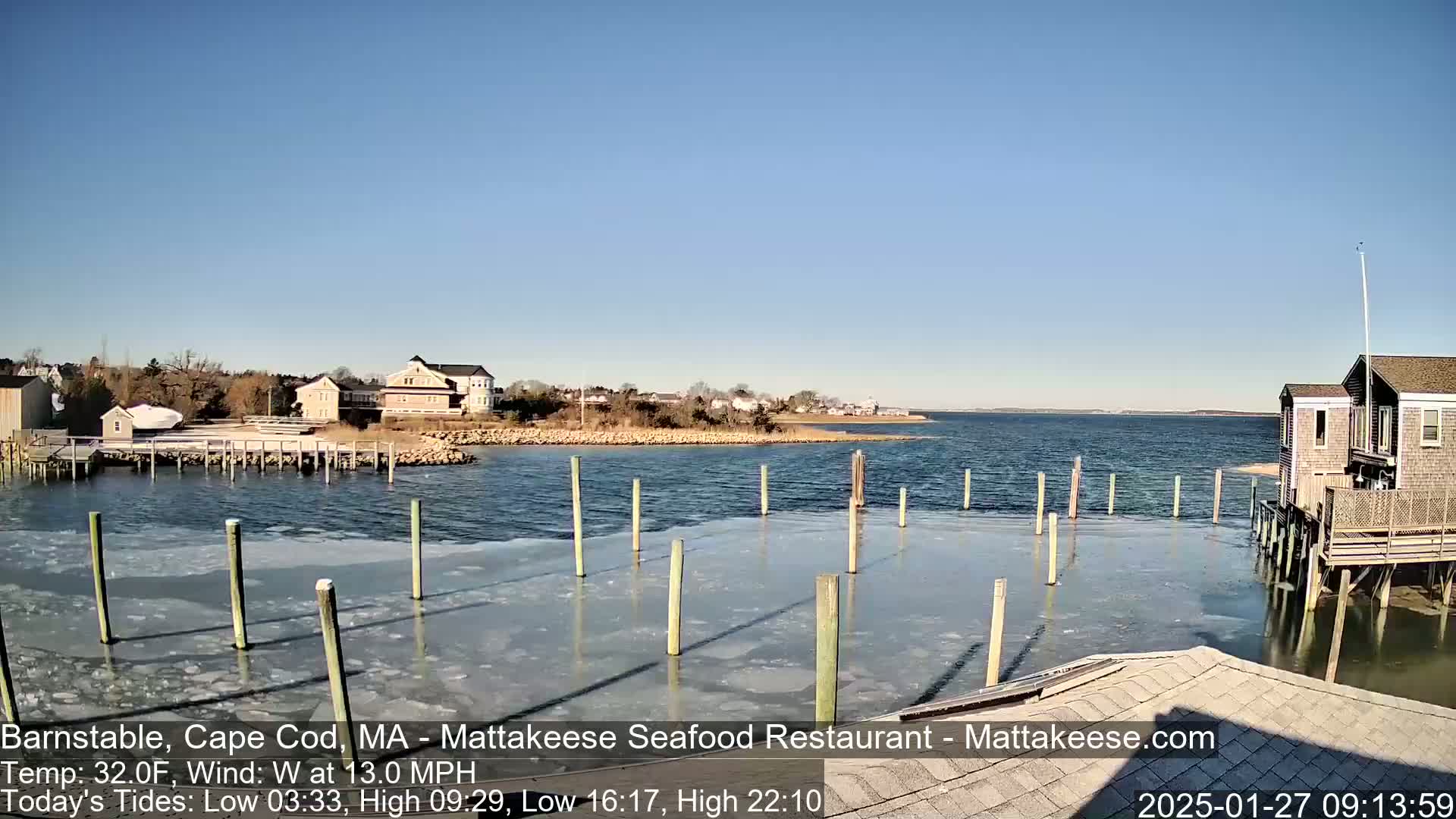 A partly frozen harbor with wooden pilings and buildings on a clear, sunny day.