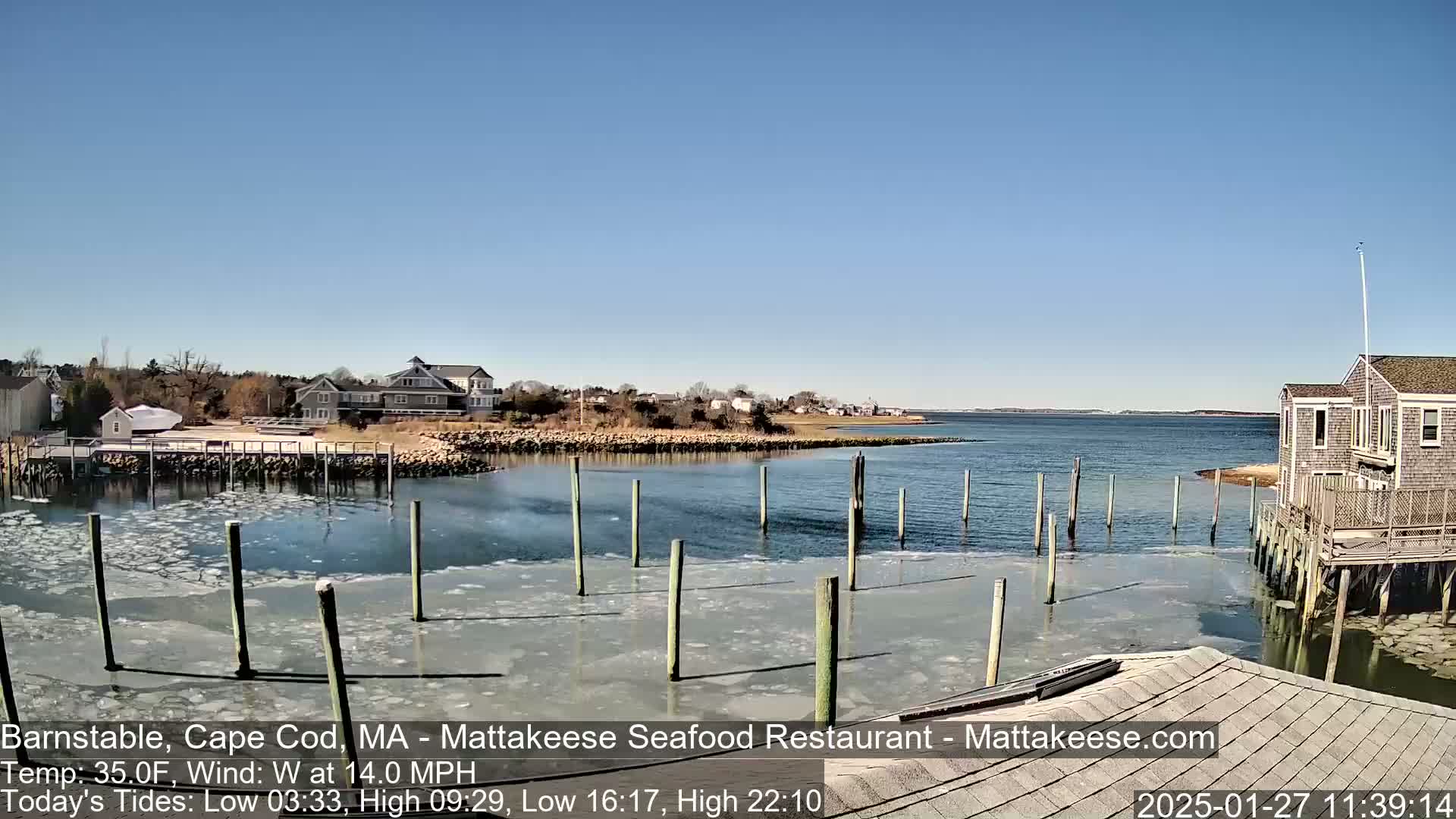 A partly frozen harbor with wooden pilings and buildings on a clear, sunny day.