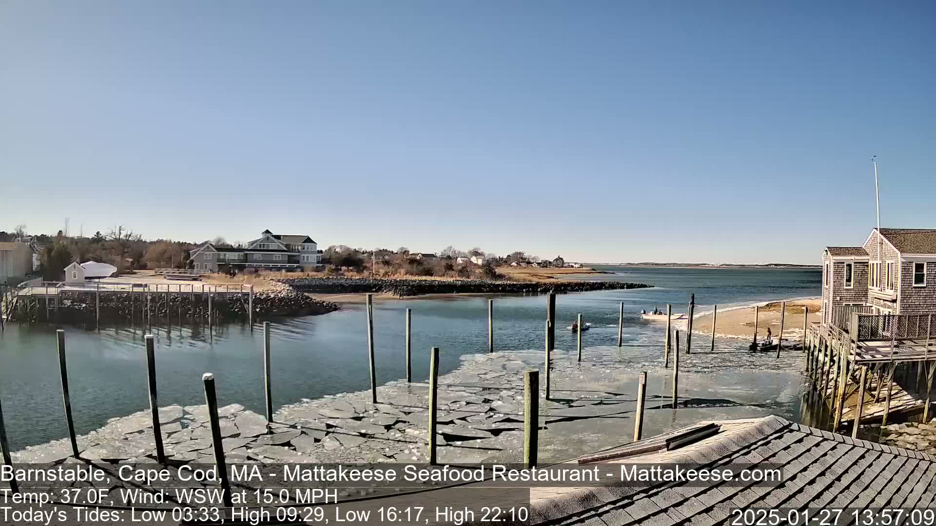 A calm, sunny day shows a harbor with broken ice in the water near a wooden dock and houses on the shore.