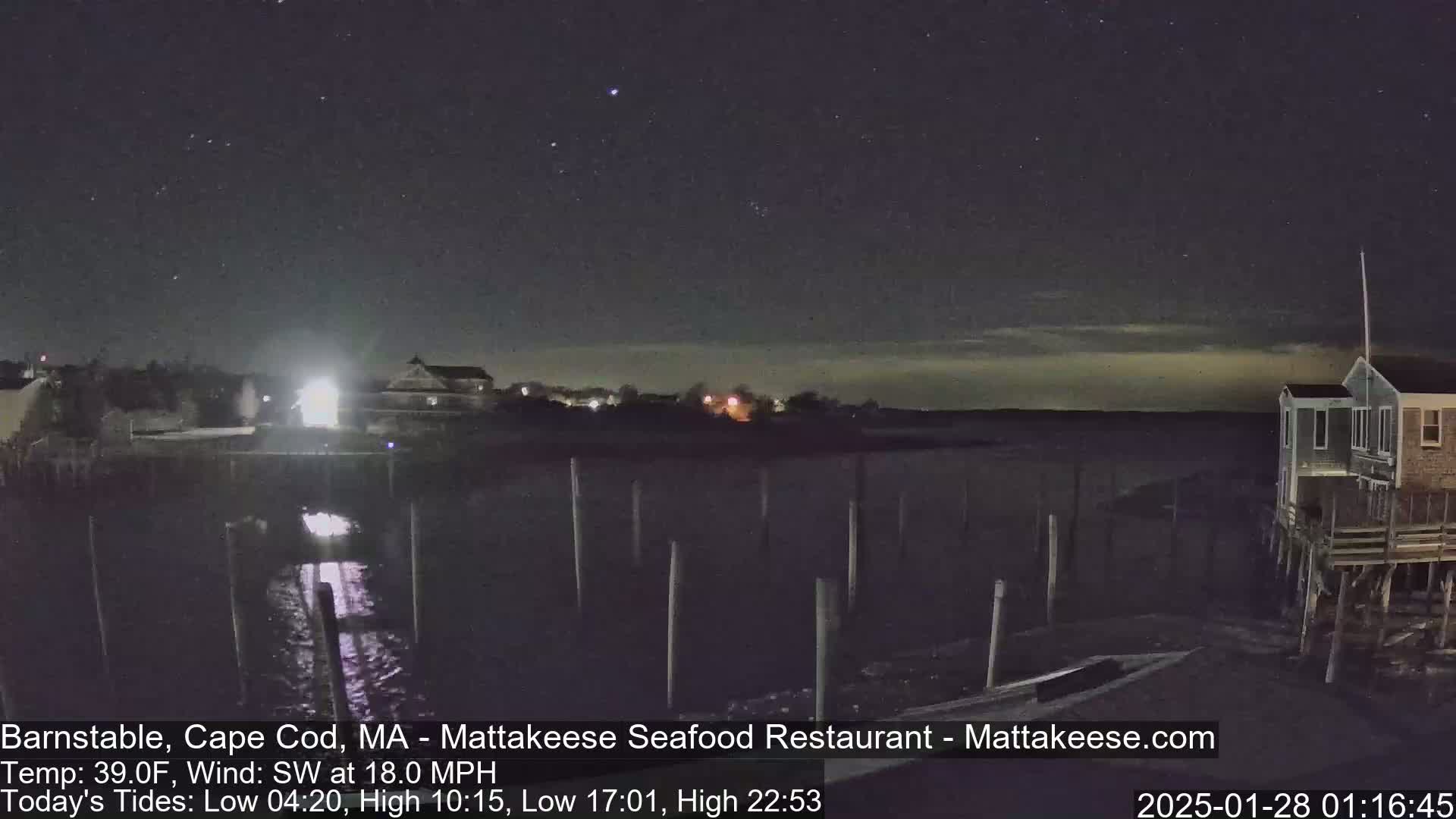 A nighttime view of a calm body of water under a partly cloudy sky, with buildings and pilings visible along the shore.