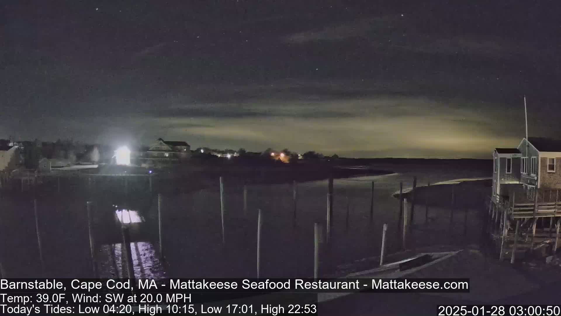 A nighttime view of a calm body of water with a few buildings and pilings visible under a slightly cloudy sky.