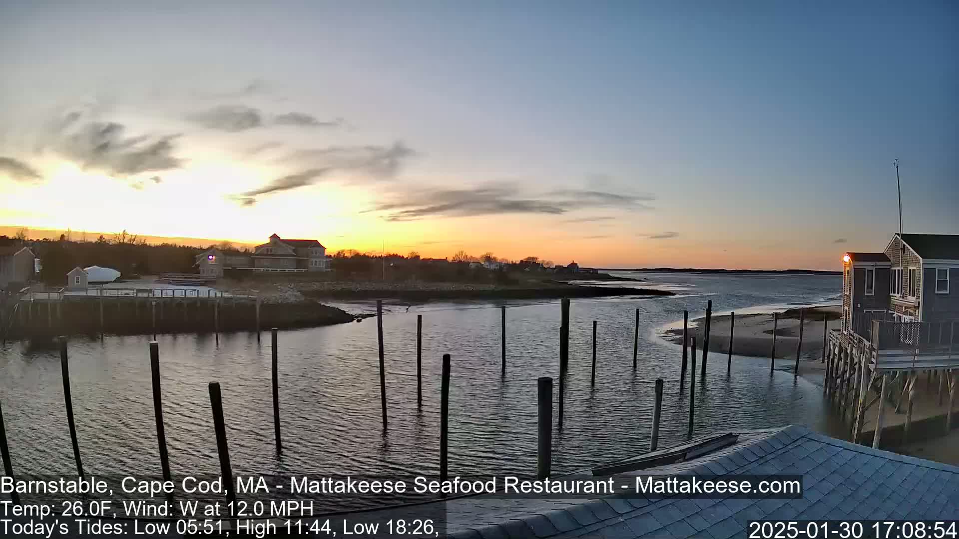 A sunset over a calm body of water, next to a small town with houses and docks, under a partly cloudy sky.