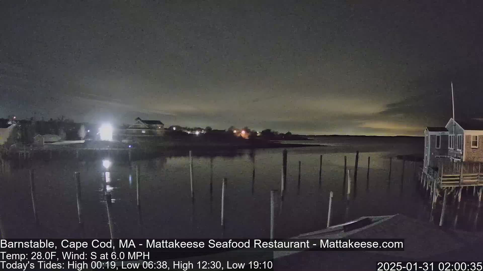 A nighttime view of a calm body of water with a few buildings and pilings visible under a dark, slightly cloudy sky.