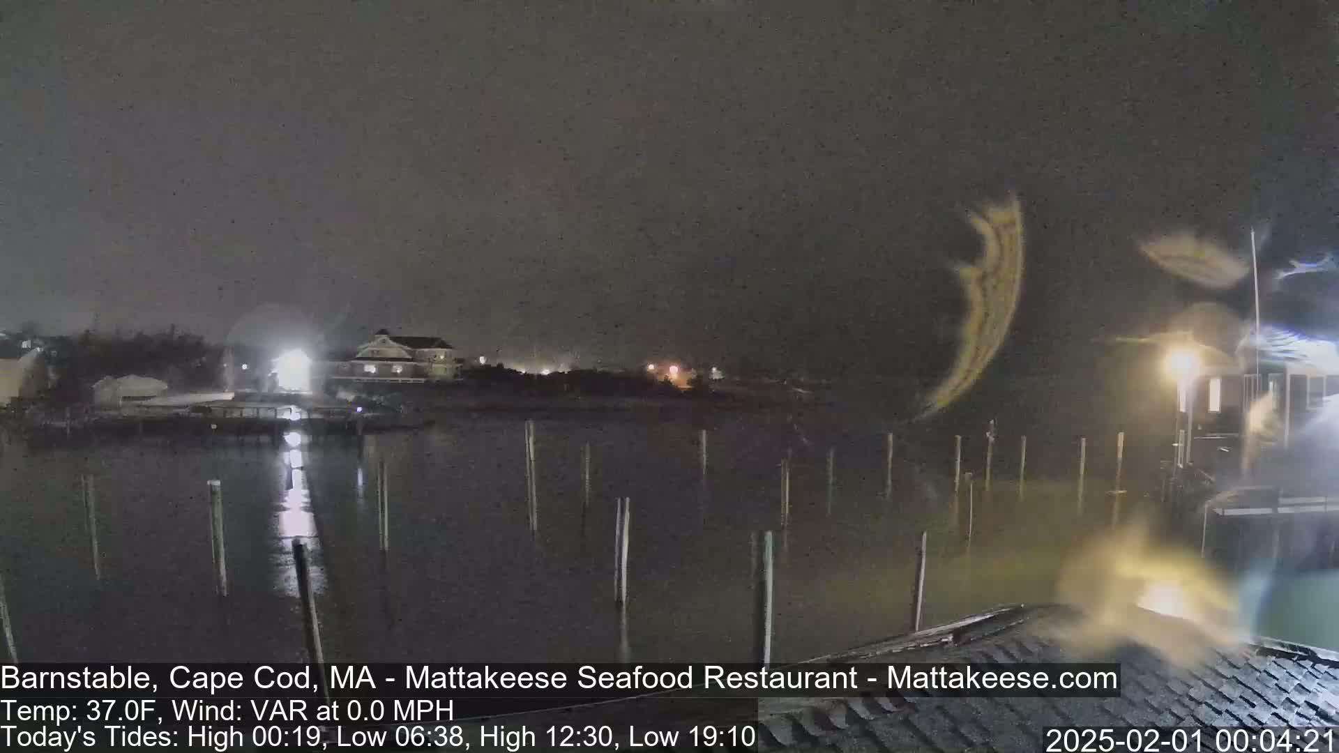 A nighttime view of a calm body of water with pilings, a building with lights, and a dark, overcast sky.